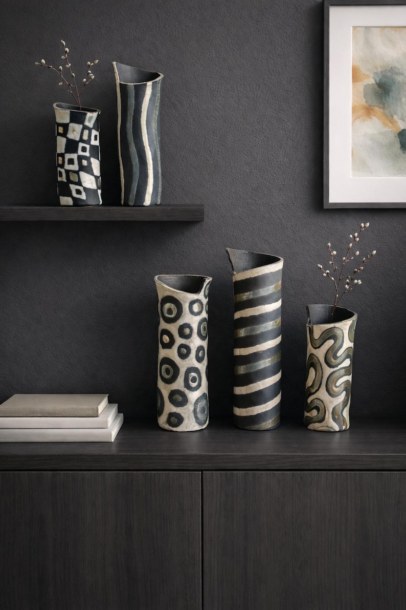 May include: A collection of ceramic vases with unique patterns. The vases feature designs such as black and white geometric shapes, stripes, and organic swirls. Some vases hold small branches, adding a natural element to the display.