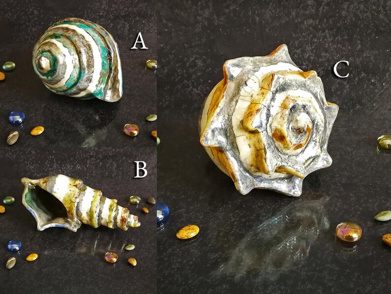 Puede incluir: Tres conchas marinas decorativas de cer&aacute;mica en varias formas y colores. Una es una espiral con rayas verdes, blancas y marrones. Otra es una concha larga y en espiral con tonos amarillos, blancos y azules. La tercera es una concha grande y texturizada con borde plateado.