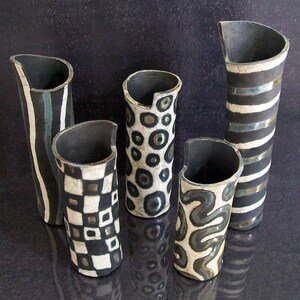 May include: Five ceramic vases with unique designs. The vases have a black interior and a variety of exterior patterns, including stripes, checks, and organic shapes in black and white. The vases are of varying heights and shapes.