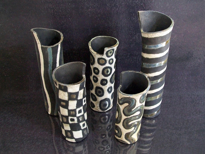May include: Five ceramic vases with unique designs. The vases have a black interior and a variety of exterior patterns, including stripes, checks, and organic shapes in black and white. The vases are of varying heights and shapes.