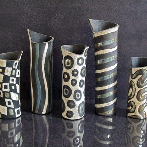 May include: Five ceramic vases with unique designs. The vases are black, white, and gray, with patterns including stripes, circles, and geometric shapes. Each vase has a slanted top and varying heights.