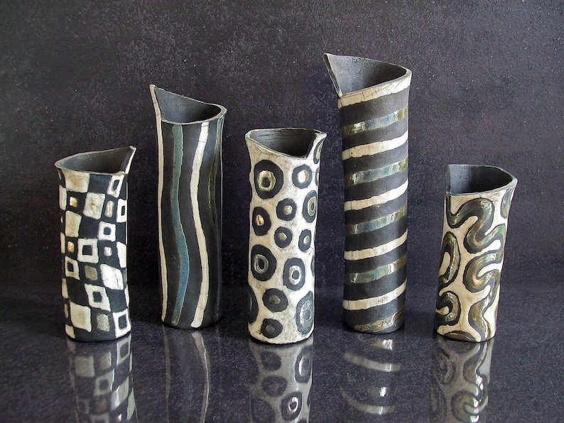 May include: Five ceramic vases with unique designs. The vases are black, white, and gray, with patterns including stripes, circles, and geometric shapes. Each vase has a slanted top and varying heights.