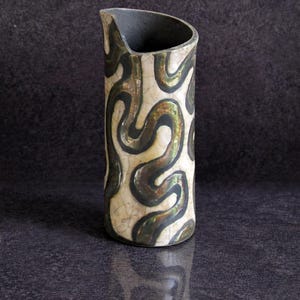May include: A ceramic pitcher with a cream-colored base and a black and gold swirling pattern. The top of the pitcher is black, and the design is reminiscent of abstract art. The pitcher is displayed on a dark surface.