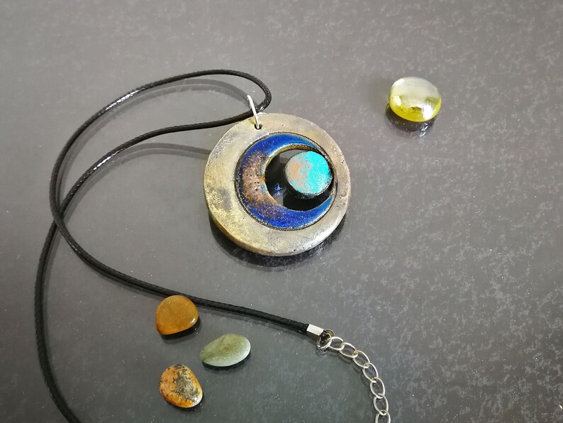 Ciondolo in ceramica Raku con tripla luna, simbolo wiccan minimalista, collana artigianale regolabile.
Raku ceramic pendant with triple moon, minimalist Wiccan symbol, adjustable handcrafted necklace.