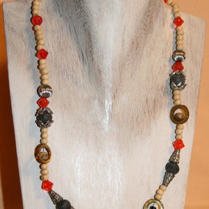 May include: A beaded necklace with a variety of elements. The necklace features wooden beads, red faceted beads, silver-colored metal beads, and dark gray stone beads. The necklace is displayed on a white mannequin.