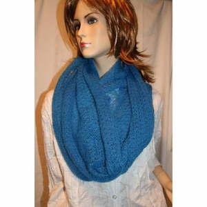 Peut inclure: Une écharpe infinie bleu vif, faite d'un matériau doux et ajouré. L'écharpe est drapée autour du cou d'un mannequin, mettant en valeur sa texture et sa couleur. L'écharpe est de couleur unie et semble faite à la main.