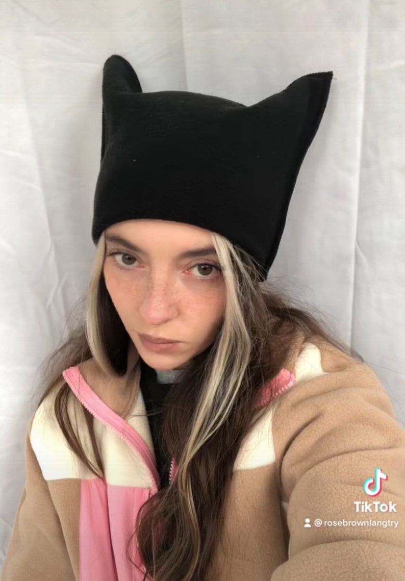 May include: A black beanie-style hat with pointed ears. The hat is worn by a person wearing a tan and pink jacket. The TikTok logo and username @rosebrownlangtry are visible in the bottom right corner.