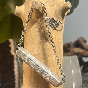 May include: A silver chain necklace with a small silver box pendant. The box is decorated with intricate floral designs and has a small silver charm attached to it.