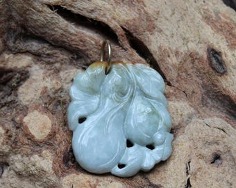 May include: A jade pendant with a carved floral design. The pendant is a pale green color with darker green and brown accents. It has a gold-colored bail for attaching to a chain. The pendant is approximately 2 inches long and 1.5 inches wide.
