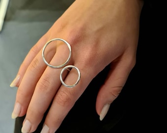 Puede incluir: Dos anillos de plata, uno más grande que el otro, se llevan en un dedo. Ambos anillos son circulares y tienen un acabado liso y pulido.