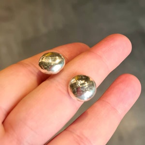 以下が含まれることがあります： ハンマーで叩いたようなテクスチャのシルバー製のイヤリングのペア。イヤリングは丸型で、滑らかで磨かれた仕上げになっています。