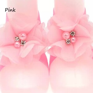 May include: Pink baby shoes with a flower design and pearl embellishments. The shoes are made of a soft, delicate fabric.