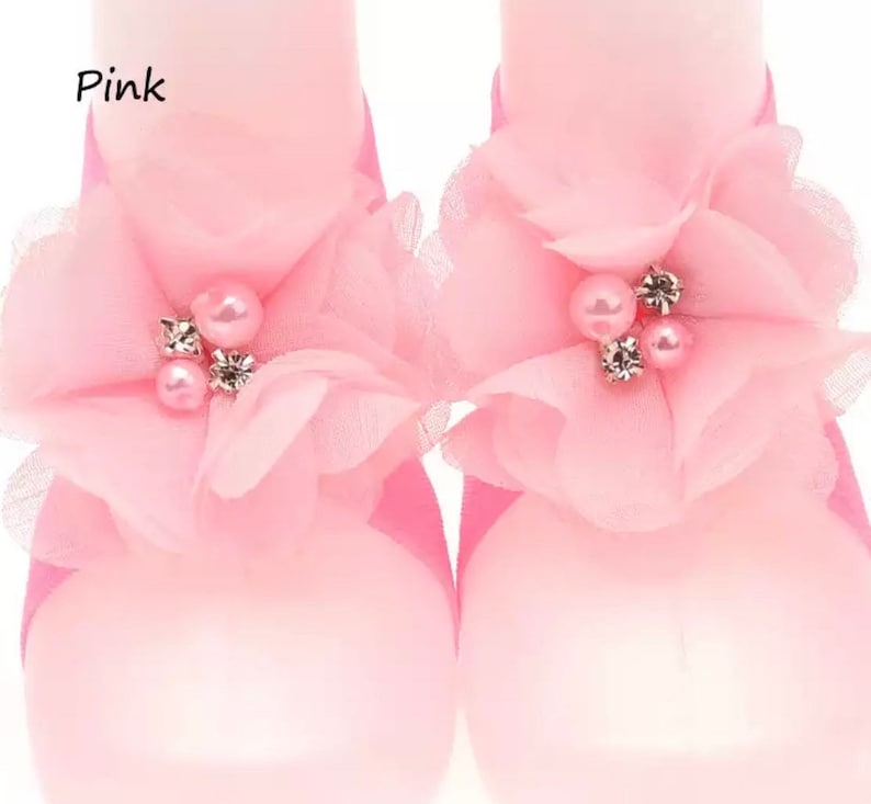 May include: Pink baby shoes with a flower design and pearl embellishments. The shoes are made of a soft, delicate fabric.