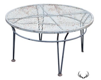 May include: A round coffee table featuring a weathered light gray metal mesh top with a visible rust patina. The table is supported by a dark gray metal frame consisting of thin, angled legs connected by a circular support ring underneath the top.