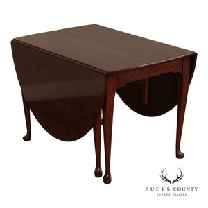 May include: A dark brown, antique drop-leaf table with a rectangular top and curved, drop-down leaves. The table has four slender, curved legs and a polished finish. The table is approximately 30 inches tall, 40 inches wide, and 20 inches deep when the leaves are down.