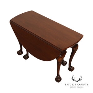 May include: A dark wood drop leaf table with a rounded edge and carved claw feet. The table is closed and the leaf is down.