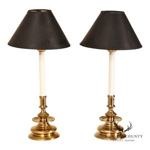 May include: A pair of table lamps featuring polished brass bases with tiered circular pedestals and white cylindrical stems. Each lamp is topped with a black conical lampshade that has a subtle textured finish. The text Bucks County Estate Traders is visible in the bottom right corner.