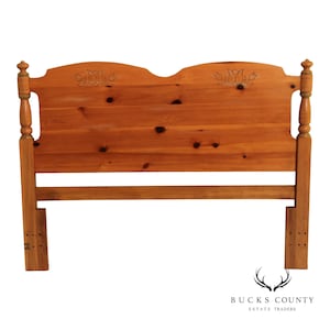 May include: A light brown wooden headboard featuring a natural wood grain with visible knots, two carved tulip motifs on the upper panel, and two vertical posts with rounded finials on each side. The structure includes a horizontal support rail.