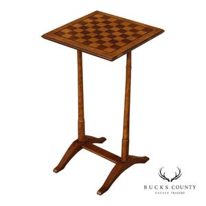 May include: A wooden chess table with a square playing surface featuring a checkerboard pattern in shades of brown. The table has a slender, adjustable stem and a four-legged base, all in a matching wood tone. The table is designed for playing chess.