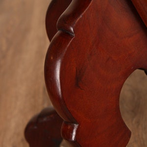 May include: Close-up of a dark mahogany wood table leg with a carved, ornate design. The leg is finished with a high gloss and has a slight curve.
