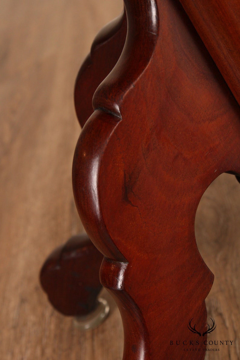 May include: Close-up of a dark mahogany wood table leg with a carved, ornate design. The leg is finished with a high gloss and has a slight curve.