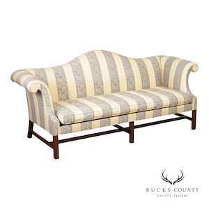 May include: A camelback sofa featuring a cream and grey striped fabric with a repeating bird and floral pattern. The sofa has rolled arms, a single long seat cushion, and a dark wood frame with straight legs connected by horizontal stretchers.