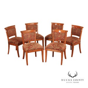 May include: A set of six wooden chairs with curved backrests and upholstered seats. Each chair features a medium brown wood frame and a patterned fabric in shades of red, green, and gold, depicting small animal figures and foliage motifs.