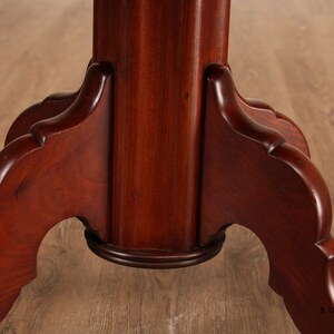 May include: Close-up of the base of a mahogany table with a turned pedestal and three legs. The legs are carved with a decorative scroll design.