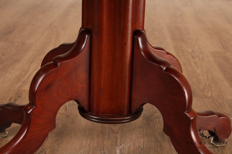 May include: Close-up of the base of a mahogany table with a turned pedestal and three legs. The legs are carved with a decorative scroll design.