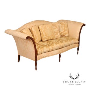 May include: A cream-colored sofa featuring a curved back, rolled arms, and dark wood legs. The upholstery displays a tonal damask pattern, complemented by four matching square throw pillows. The frame is accented with dark wood trim along the front.