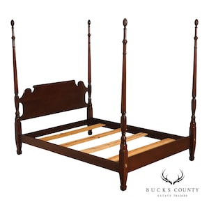 May include: A dark brown wooden four-poster bed frame featuring a headboard with a curved top edge and four tall, slender posts topped with decorative finials. The frame includes side rails and horizontal wooden slats for mattress support.