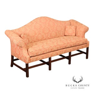 May include: A camelback sofa upholstered in a peach-colored fabric with a tonal damask pattern. The sofa features rolled arms, a single seat cushion, two small square throw pillows, and a dark wood base with straight legs and stretchers.