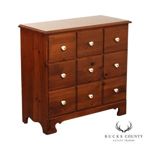 May include: A wooden chest of drawers with nine drawers, each with a white knob. The chest is made of dark brown wood and has a rectangular shape. The chest is a classic piece of furniture.