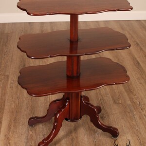 May include: A three-tiered mahogany table with a scalloped edge on each shelf. The table has a turned pedestal base with four carved legs.