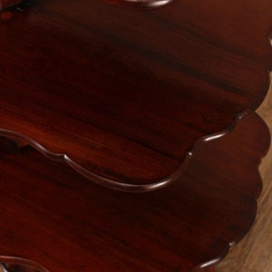 May include: A three-tiered mahogany wood table with scalloped edges on each tier. The table has a dark, rich finish and is supported by four turned legs.