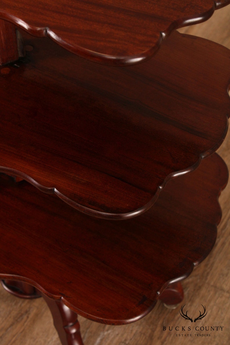 May include: A three-tiered mahogany wood table with scalloped edges on each tier. The table has a dark, rich finish and is supported by four turned legs.