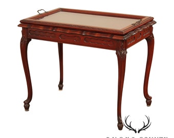 May include: A mahogany wood end table with a glass top and carved details. The table has four legs with a cabriole design and a brass handle on the top.