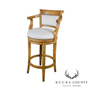 May include: A wooden bar stool with a white upholstered seat and back. The stool has a curved back and a single armrest. The stool is made of light wood with a natural finish.