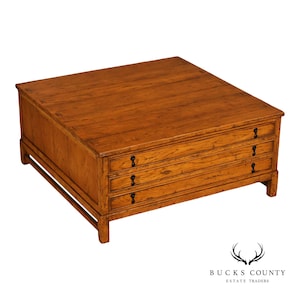 May include: A square wooden coffee table with a warm brown finish, featuring a flat top surface and three horizontal drawers stacked vertically on the front side. Each drawer is equipped with a small, dark metal pull handle for opening.