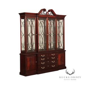 May include: A mahogany china cabinet with glass doors and a decorative top. The cabinet has a lower section with drawers and doors.