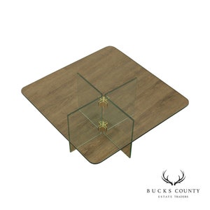 May include: A square glass coffee table with a wood top and brass accents. The glass panels are held together by brass connectors in the shape of a star.