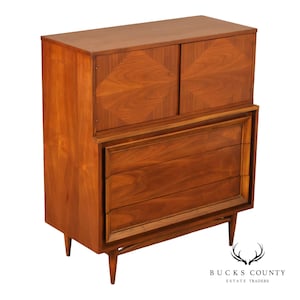 May include: A tall wooden chest of drawers featuring a rectangular top, two upper cabinet doors with a diamond-patterned wood grain, and three lower drawers with recessed handles. The piece is supported by four tapered, angled wooden legs.