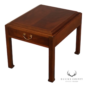 May include: A rectangular wooden side table with a rich brown finish, featuring a single drawer with a curved brass pull handle. The table has a flat top surface with a raised border and four straight legs that flare slightly at the base.