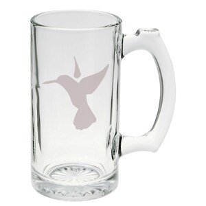 May include: A clear glass mug with a frosted hummingbird design. The mug has a handle and a wide base.