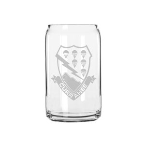 Puede incluir: Una lata de vidrio transparente con un diseño grabado en blanco de un escudo con un rayo y paracaídas. El texto "CURRAHEE" está escrito en una pancarta debajo del escudo.