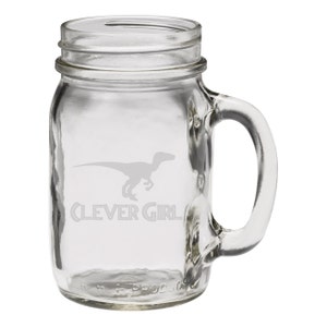 Op de afbeelding: Een heldere glazen mason jar mok met een handvat. De mok heeft een silhouet van een dinosaurus en de tekst "Clever Girl" geëtst in het glas.