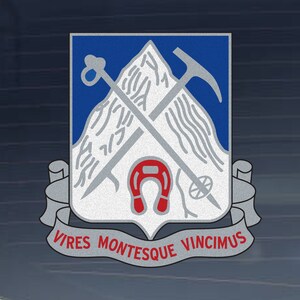 May include: A silver and blue crest featuring a mountain, crossed ice axes, and a red horseshoe. The crest is surrounded by a silver ribbon with the text "Vires Montesque Vincimus".