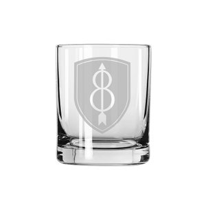 Puede incluir: Un vaso de vidrio transparente con un diseño grabado de un escudo gris con una flecha y un número ocho estilizado en su interior.