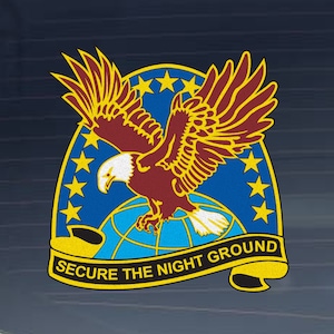 May include: A blue and yellow emblem featuring a red-tailed eagle soaring above a globe. The eagle has a white head and a yellow beak. The globe is encircled by a ring of stars. The text "SECURE THE NIGHT GROUND" is displayed on a yellow banner.