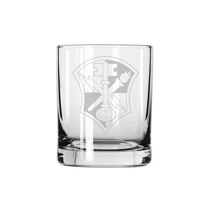 May include: A clear glass tumbler with an etched design of a military insignia. The insignia features a key, a torch, and a lightning bolt.